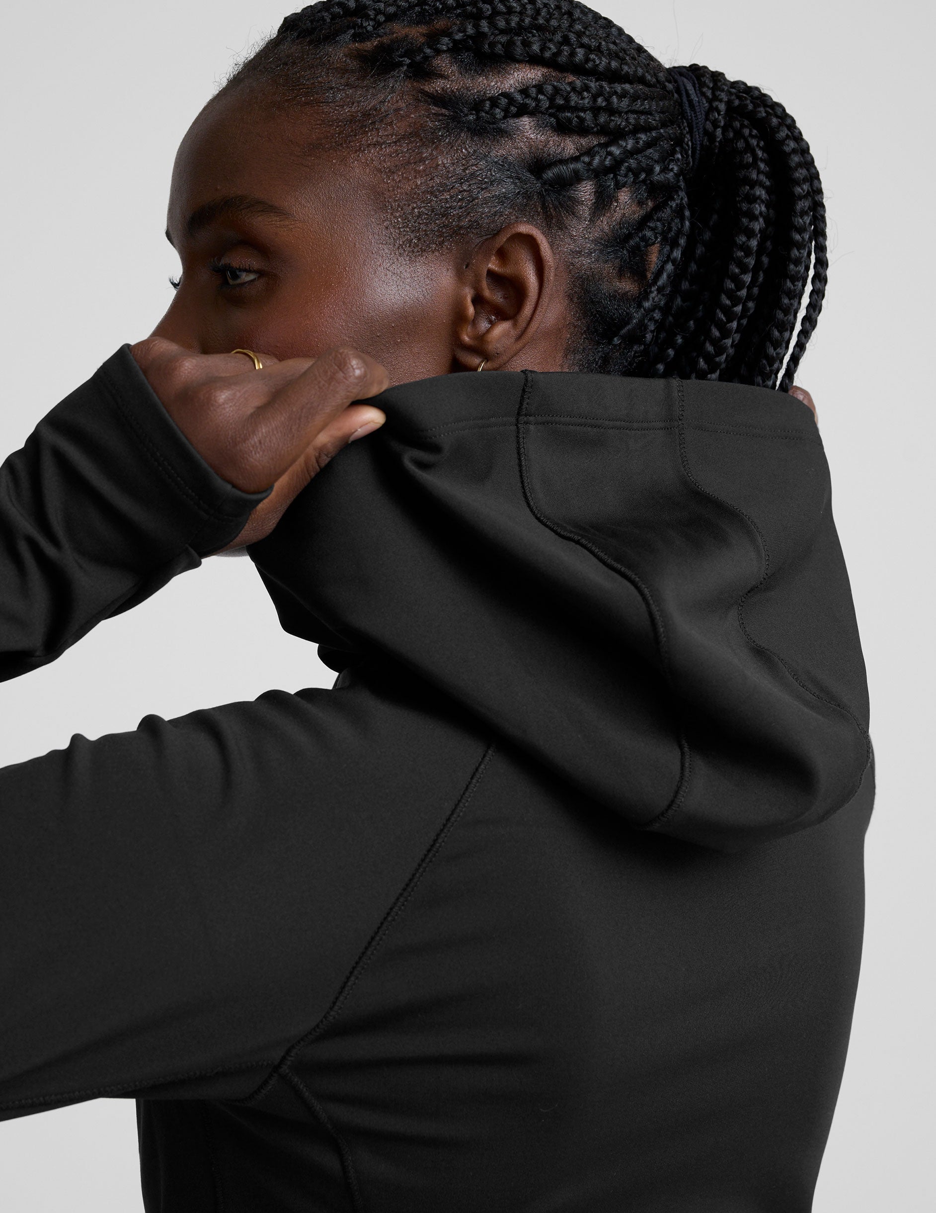 woman in black zip-up hooded jacket and leggings against a plain background.