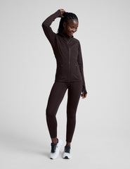 Woman wearing a brown full zip fleece lined jacket and leggings against a light gray background.