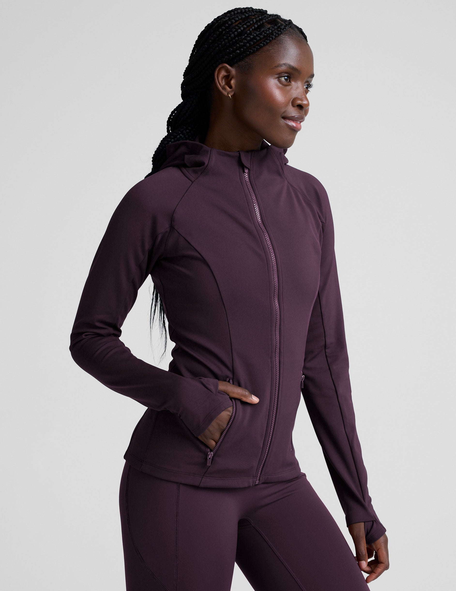 woman wearing a purple hooded jacket and leggings on a plain background.