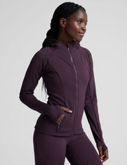 woman wearing a purple hooded jacket and leggings on a plain background.