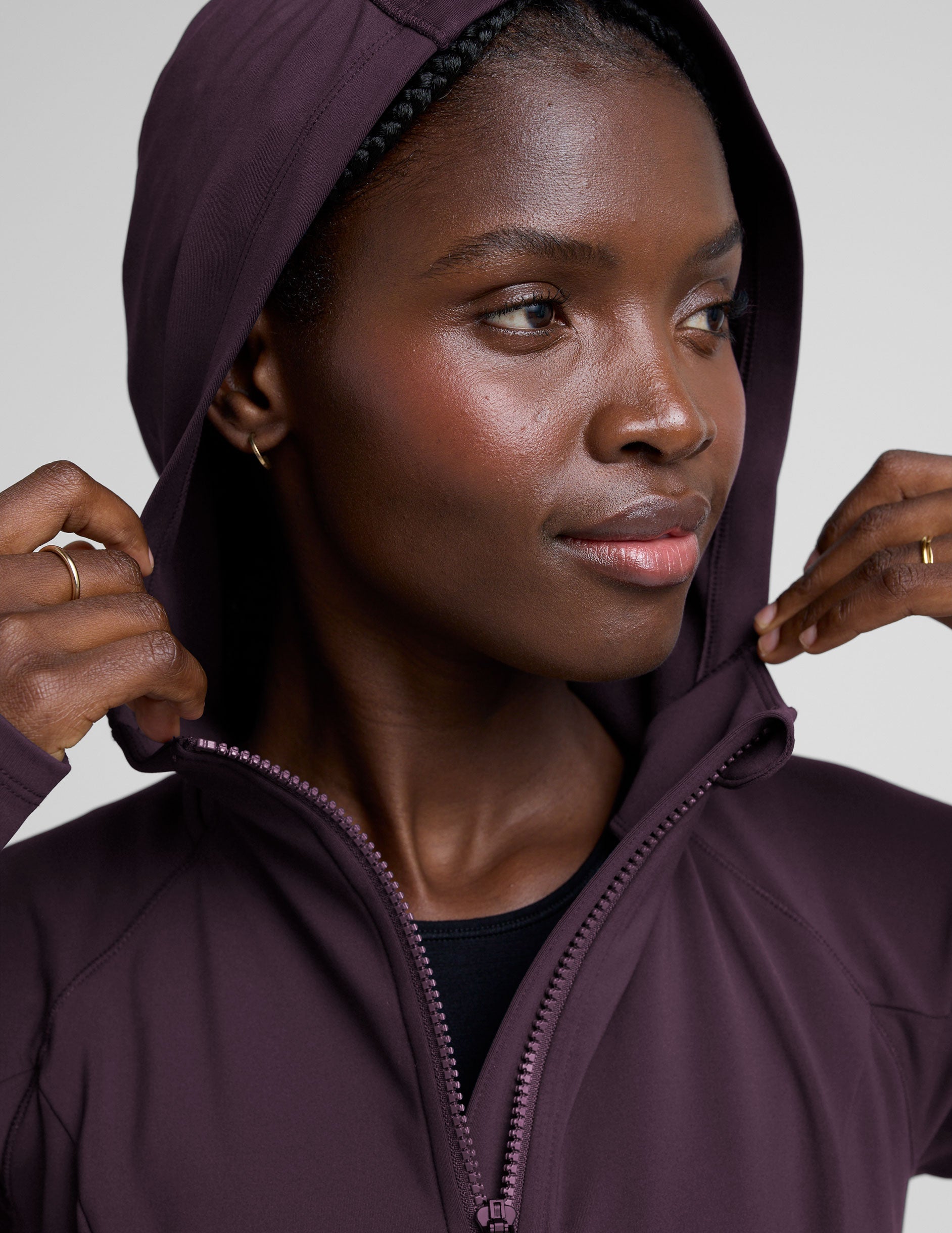 woman wearing a purple hooded jacket and leggings on a plain background.