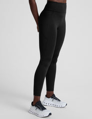 woman wearing a black high-waisted long length leggings with pockets athletic outfit on a plain background.