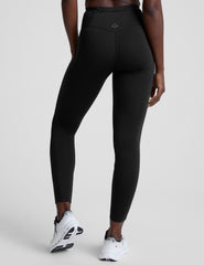 woman wearing a black high-waisted long length leggings with pockets athletic outfit on a plain background.