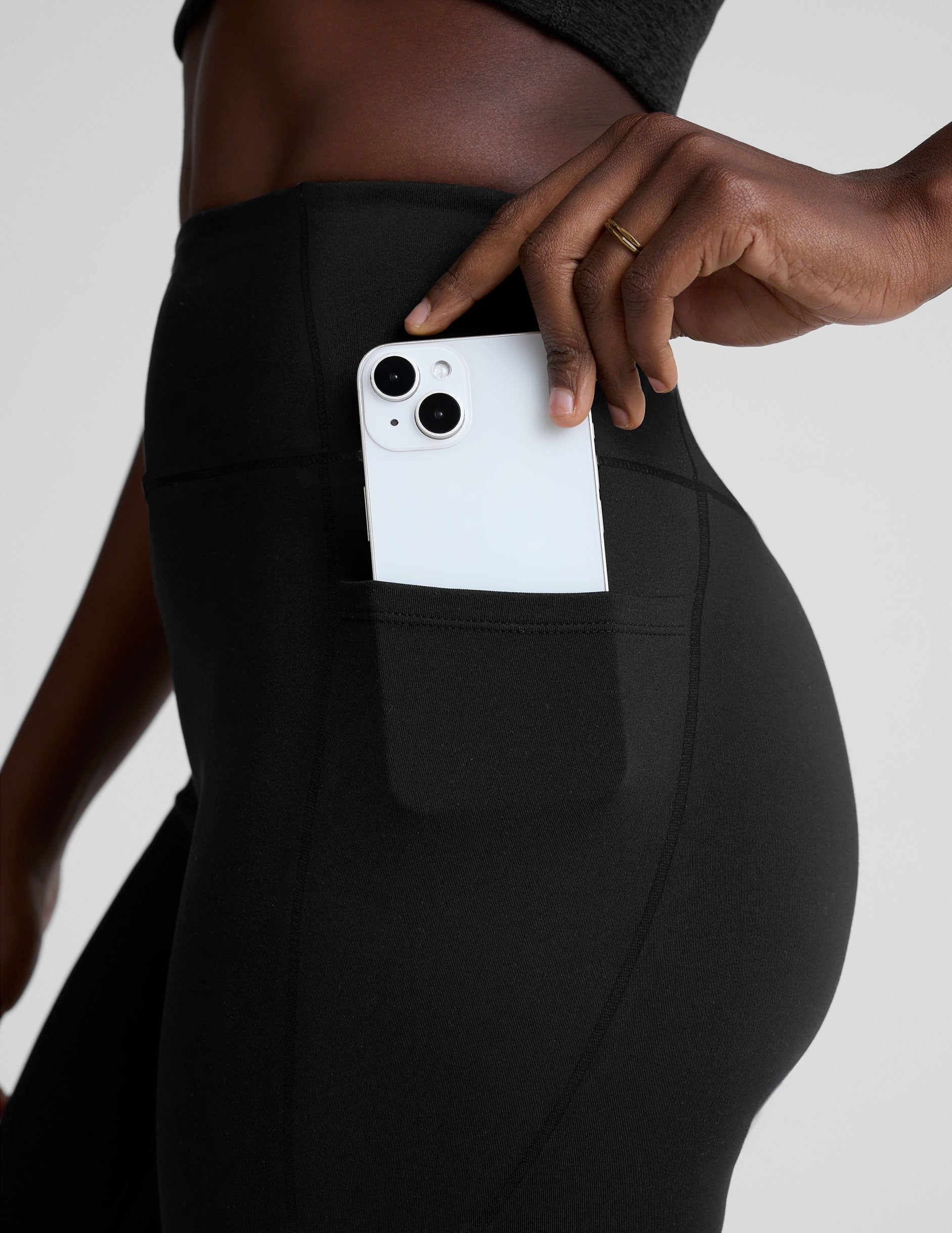 woman wearing a black high-waisted long length leggings with pockets athletic outfit on a plain background.