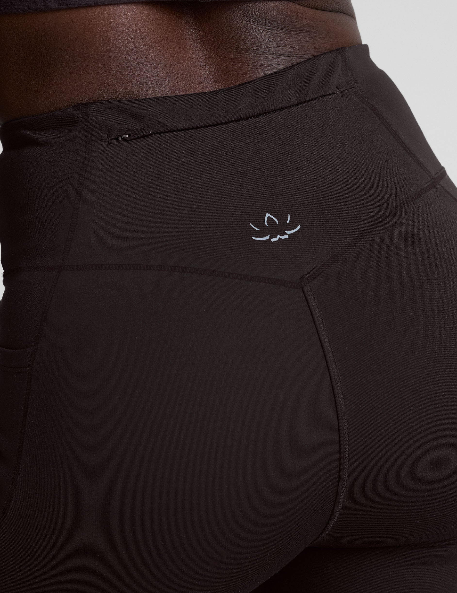 person wearing brown high-waisted long leggings with pockets on a plain background.