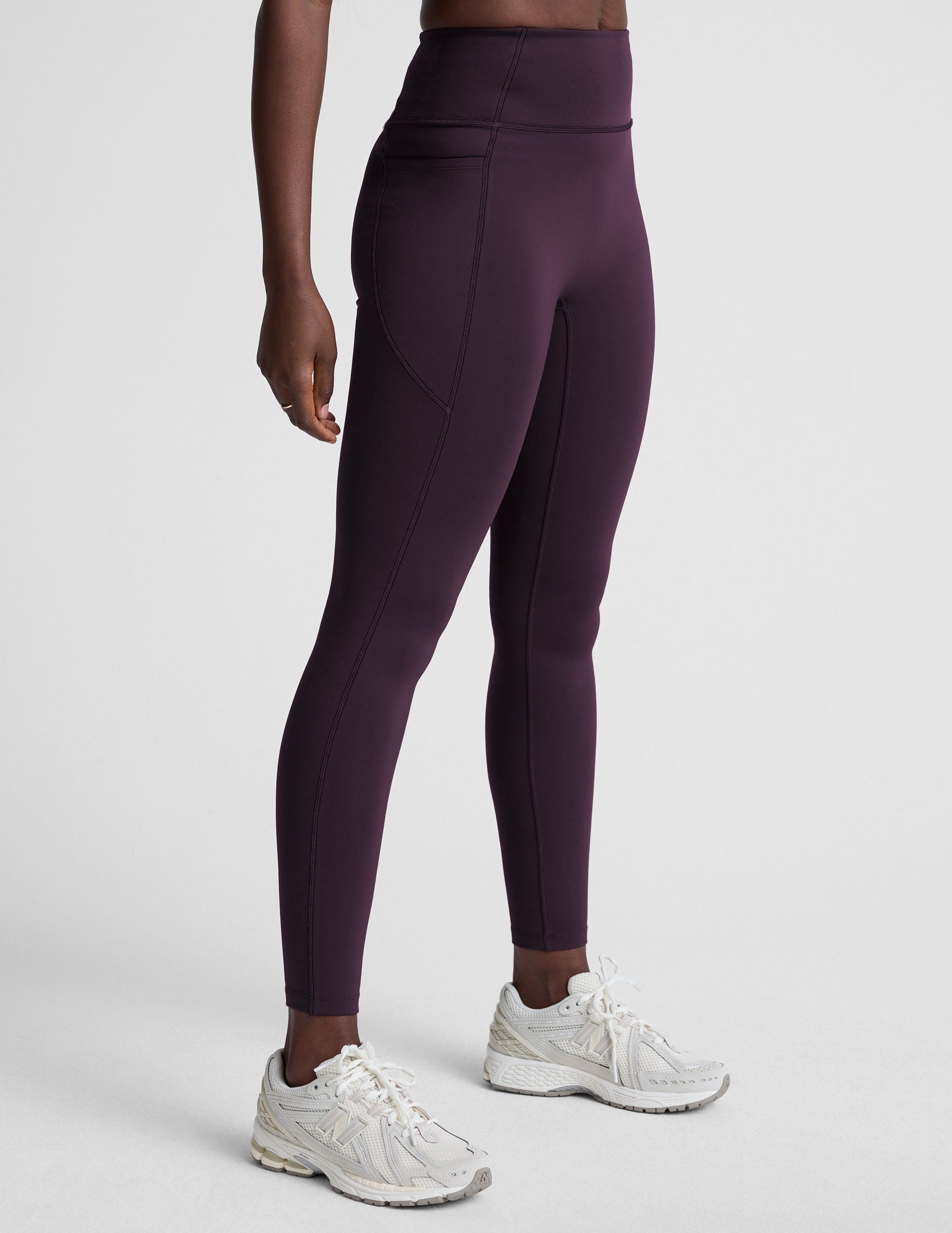 woman wearing high-waisted purple long length leggings with pockets against a plain background.