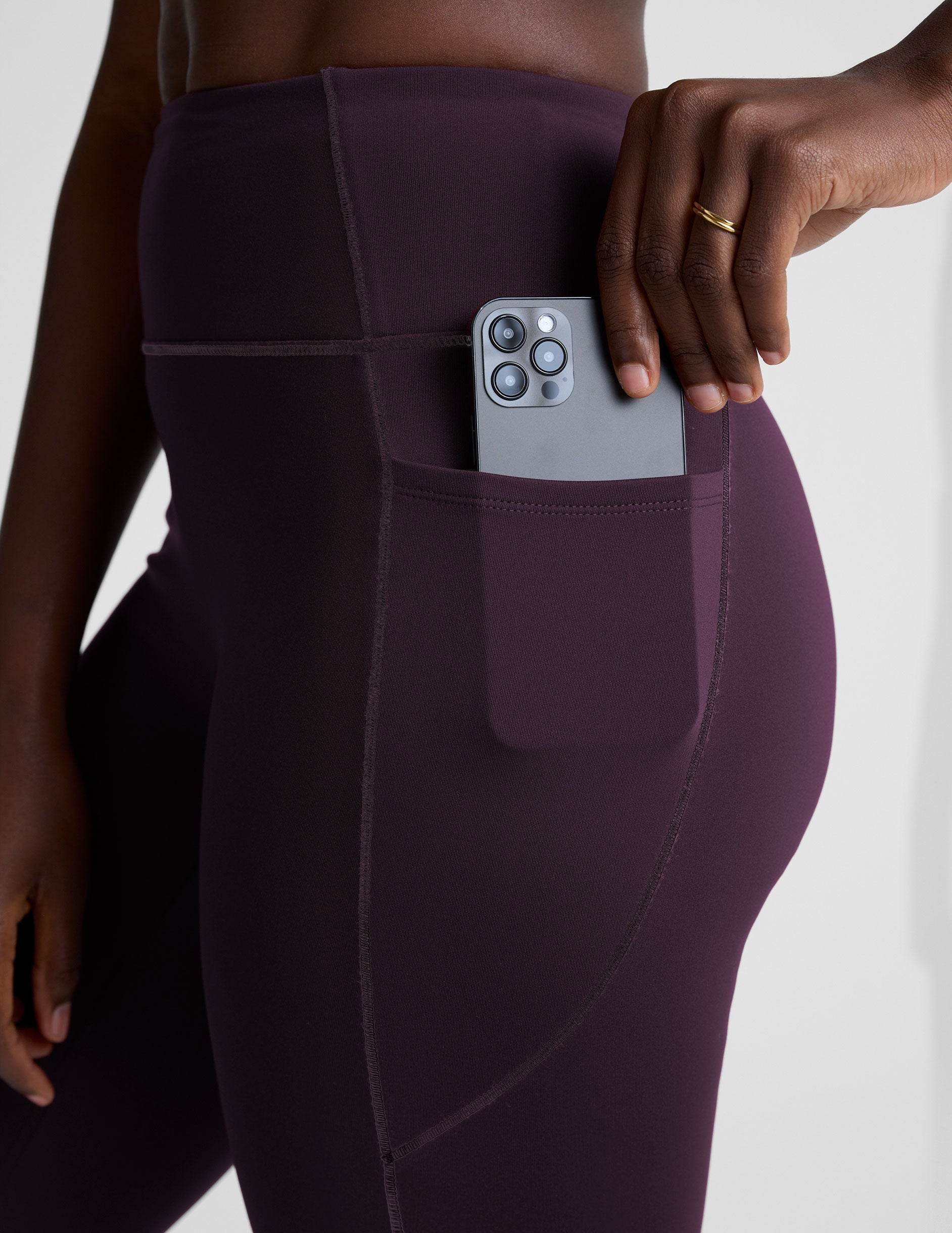 woman wearing high-waisted purple long length leggings with pockets against a plain background.