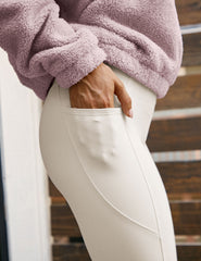 close-up of a person wearing a pink fleece jacket and white leggings with a blurred background.
