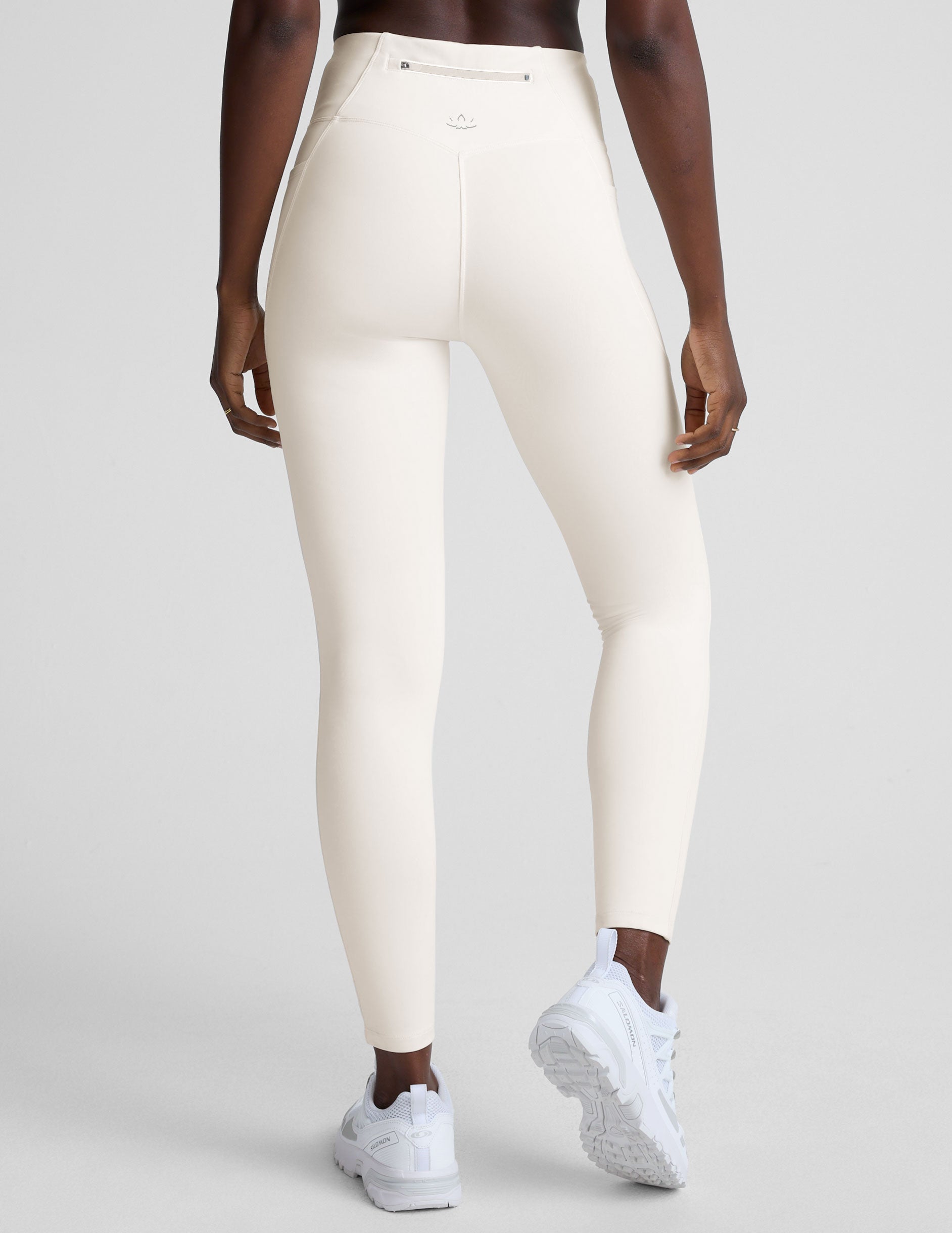 woman wearing white high-waisted long length leggings with pockets on a plain background.