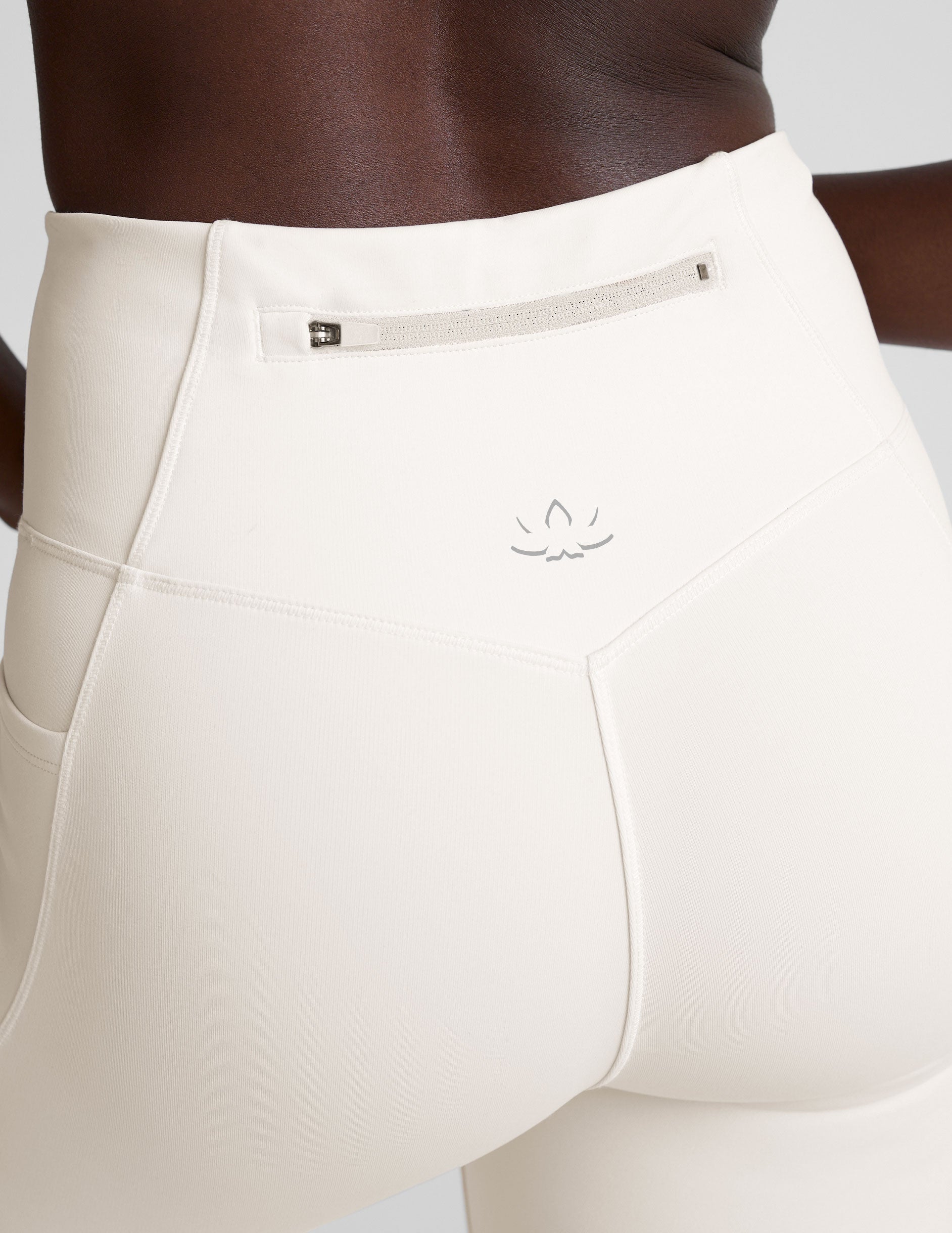 woman wearing white high-waisted long length leggings with pockets on a plain background.