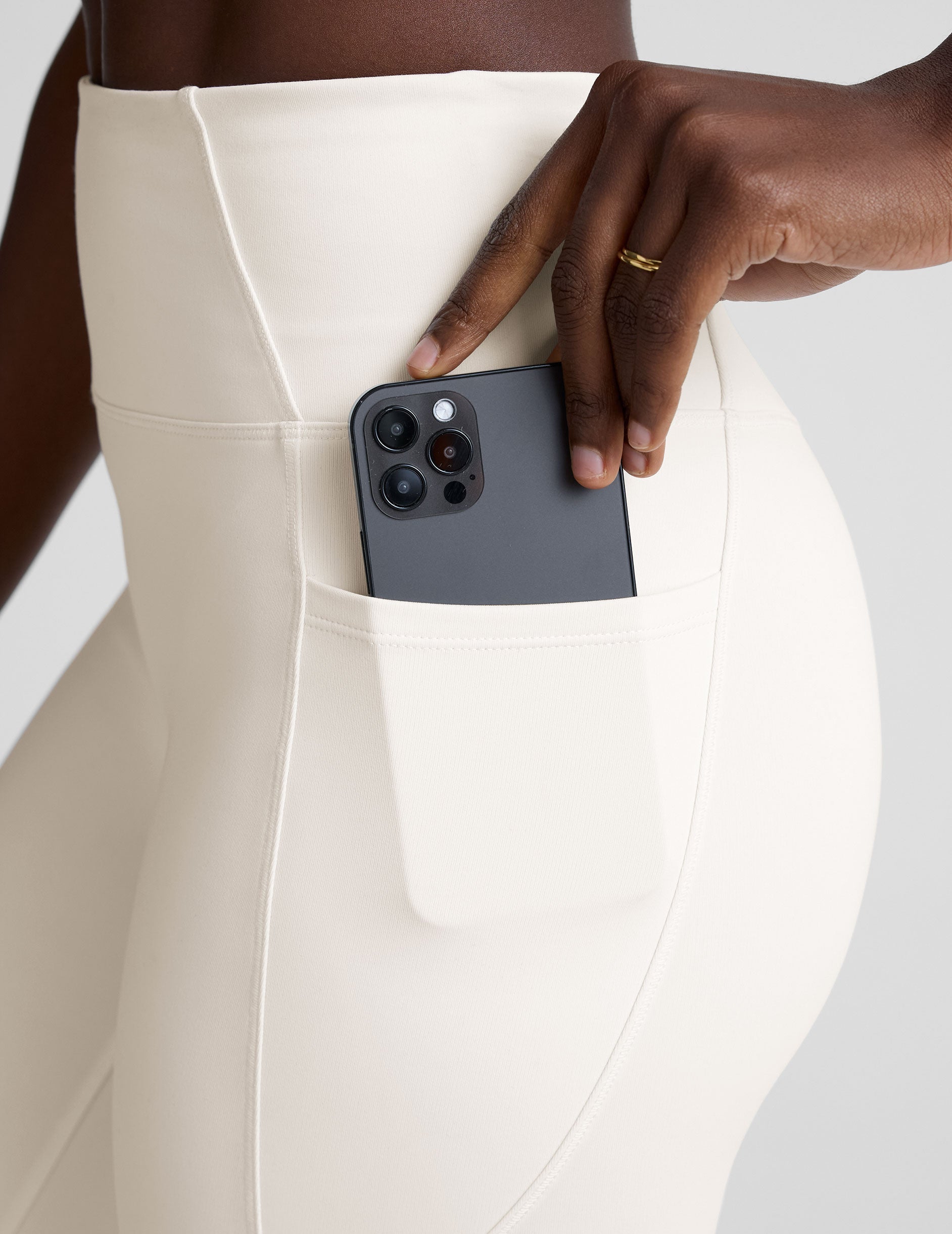 woman wearing white high-waisted long length leggings with pockets on a plain background.