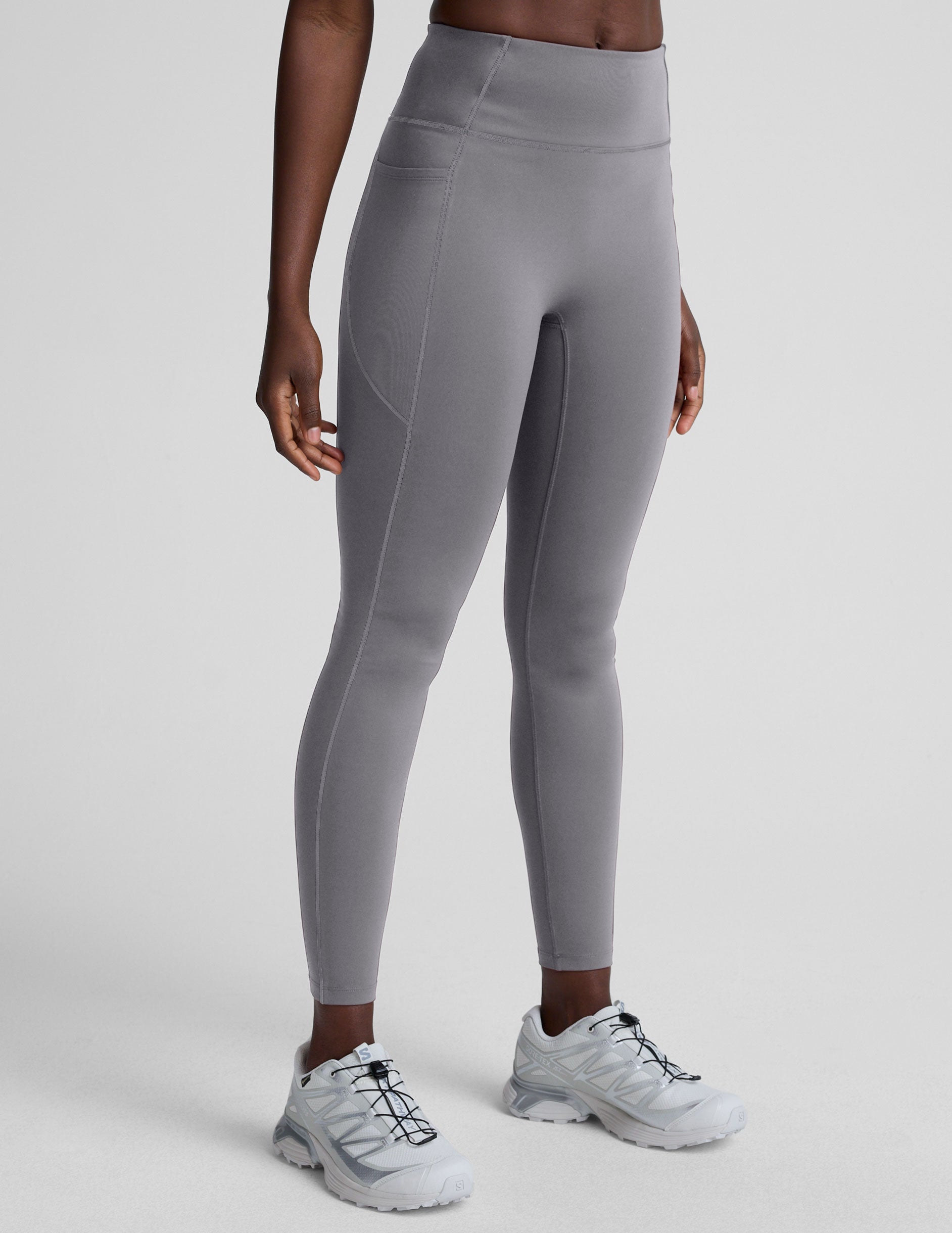 woman wearing gray high-waisted long length leggings on a plain background.