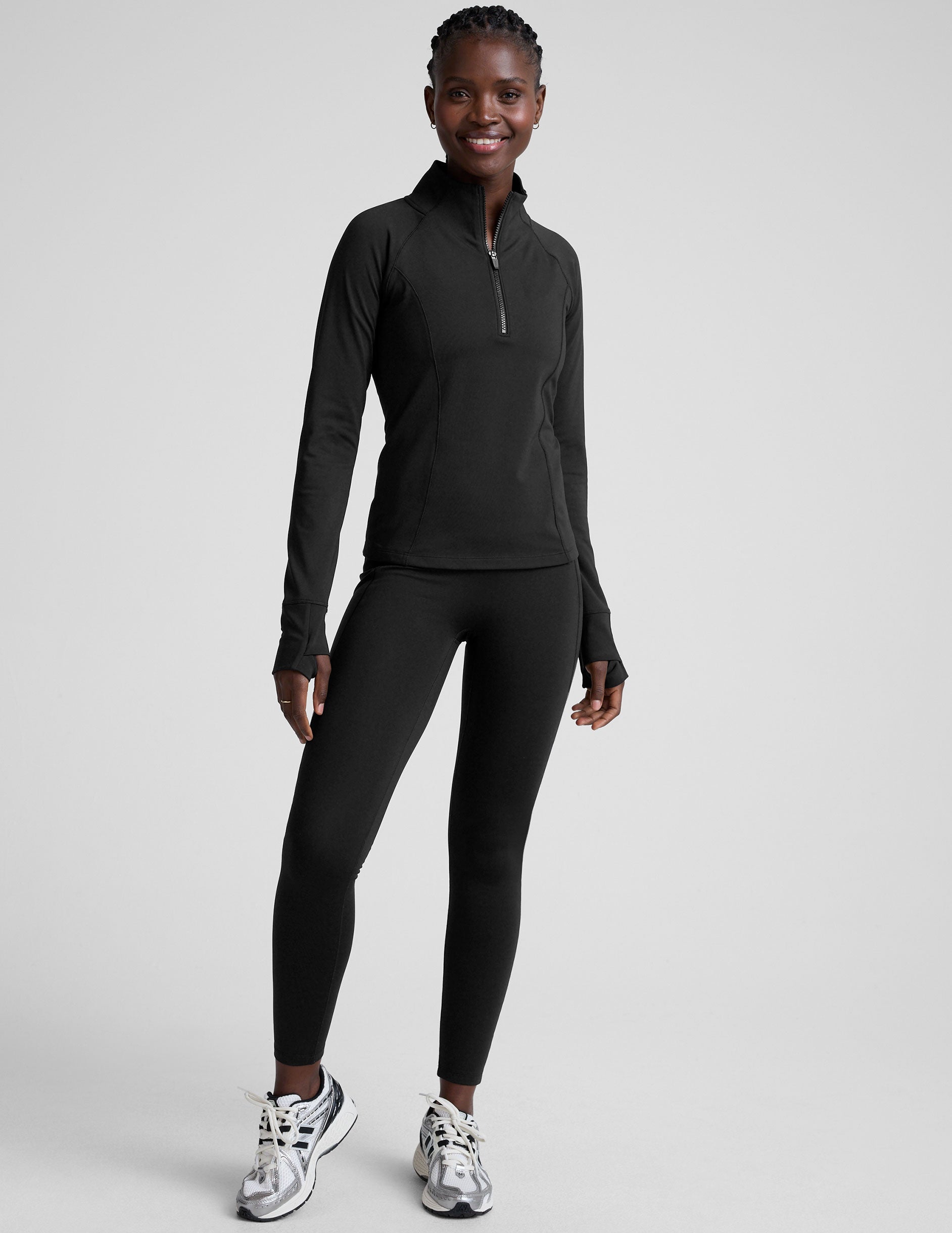 woman wearing a black long-sleeve athletic jacket with a zipper on a plain background.