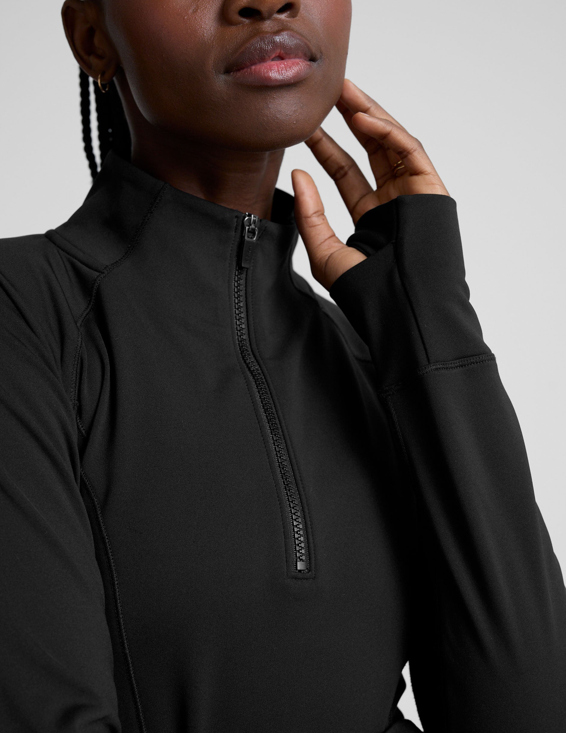 woman wearing a black long-sleeve athletic jacket with a zipper on a plain background.