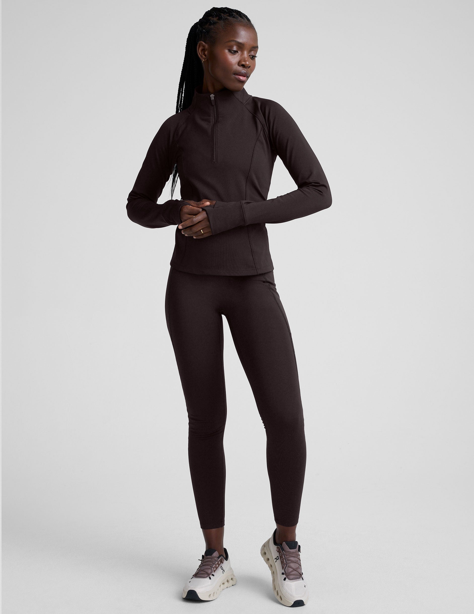 woman wearing a brown quarter-zip jacket and leggings on a plain background.