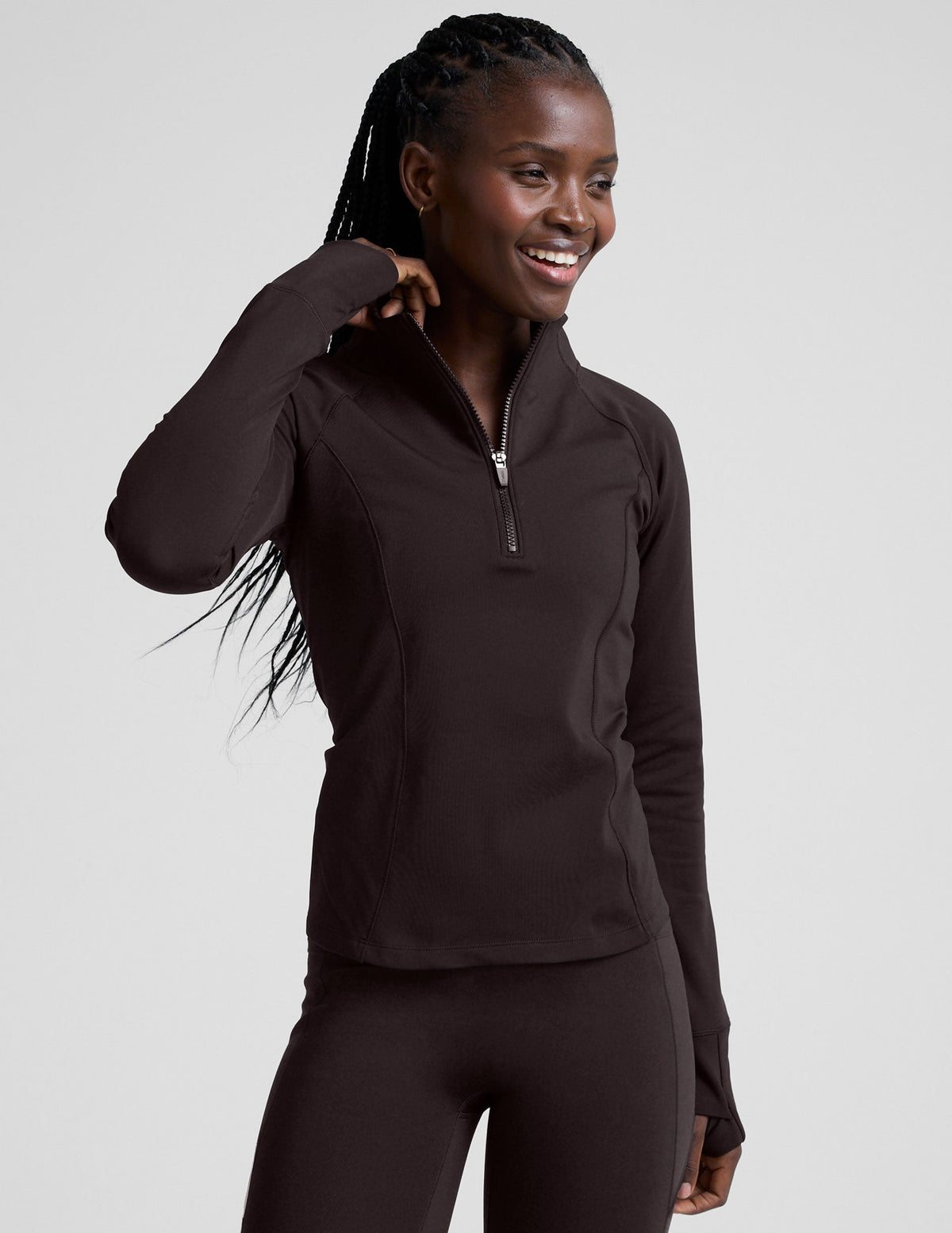 woman wearing a brown quarter-zip jacket and leggings on a plain background.