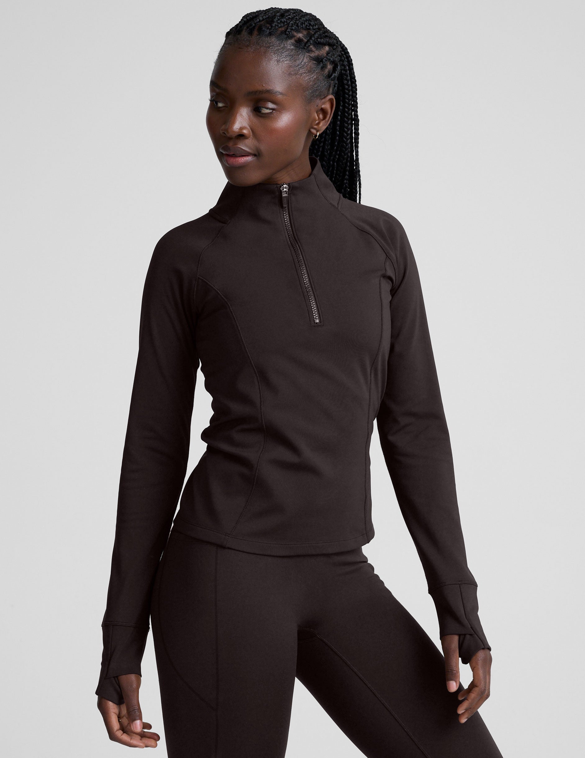 woman wearing a brown quarter-zip jacket and leggings on a plain background.