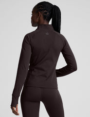 woman wearing a brown quarter-zip jacket and leggings on a plain background.