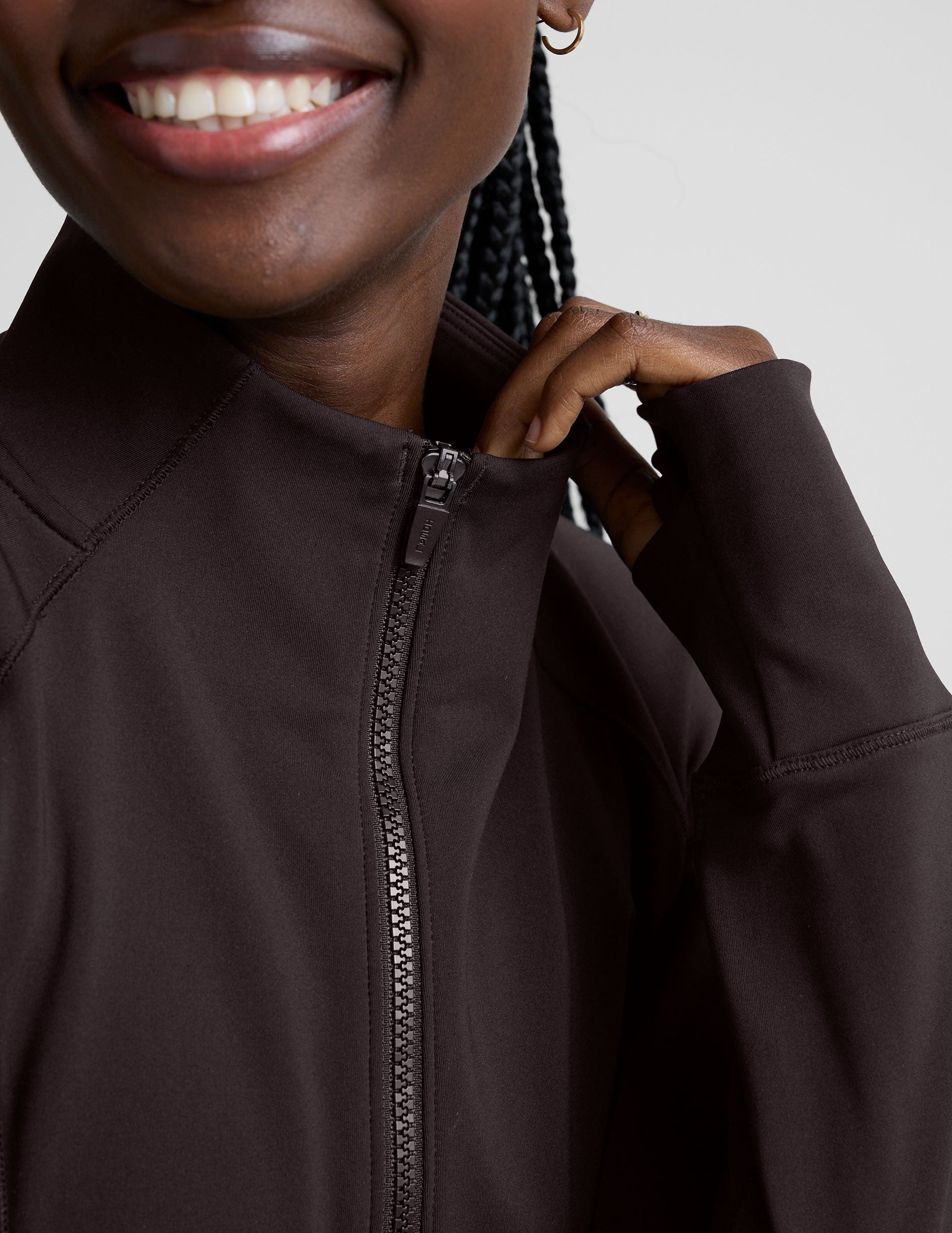 woman wearing a brown quarter-zip jacket and leggings on a plain background.