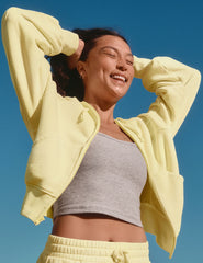 model in a yellow jacket and gray top against a clear blue sky.