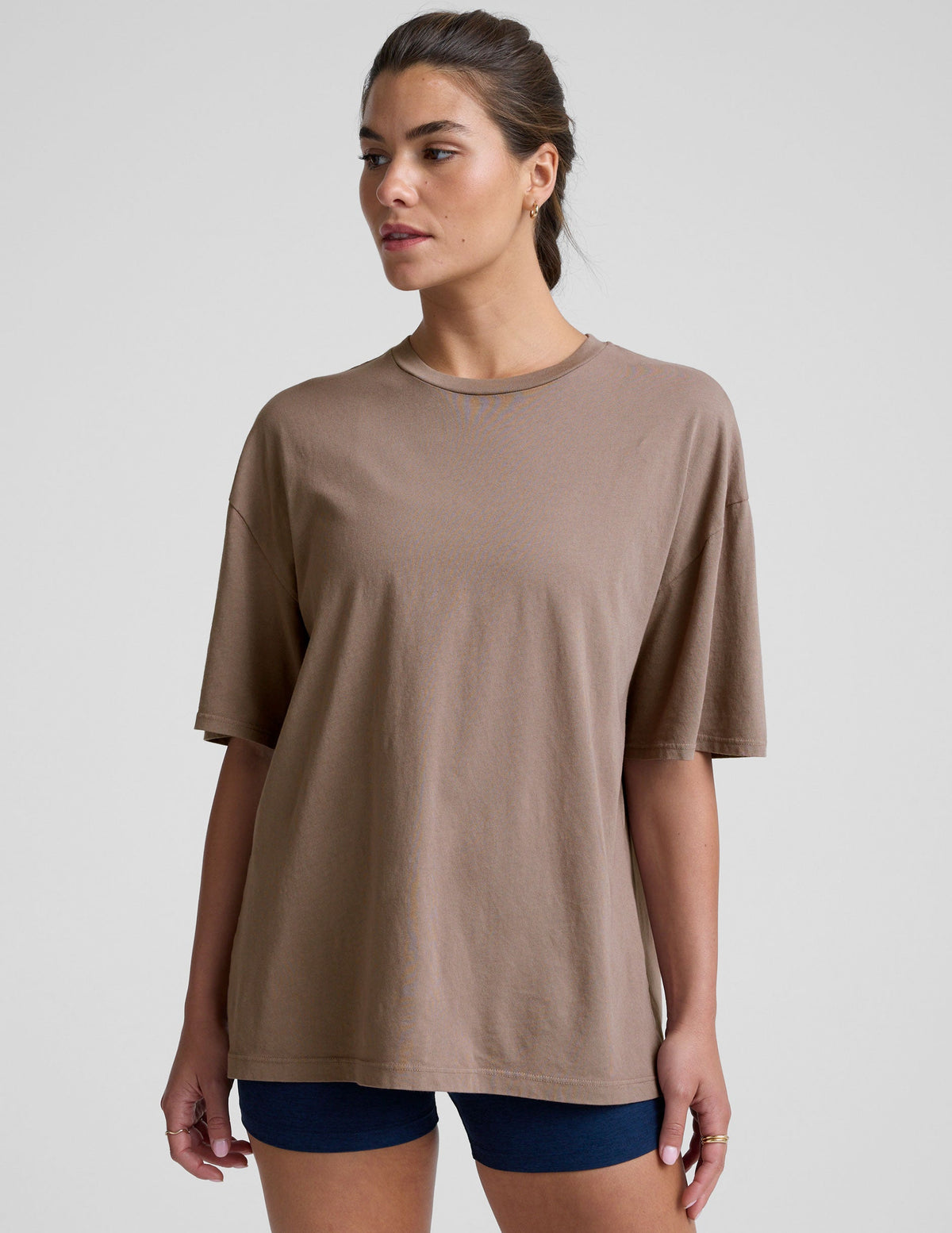 model wearing a brown oversized cotton t-shirt and navy shorts on a light gray background.