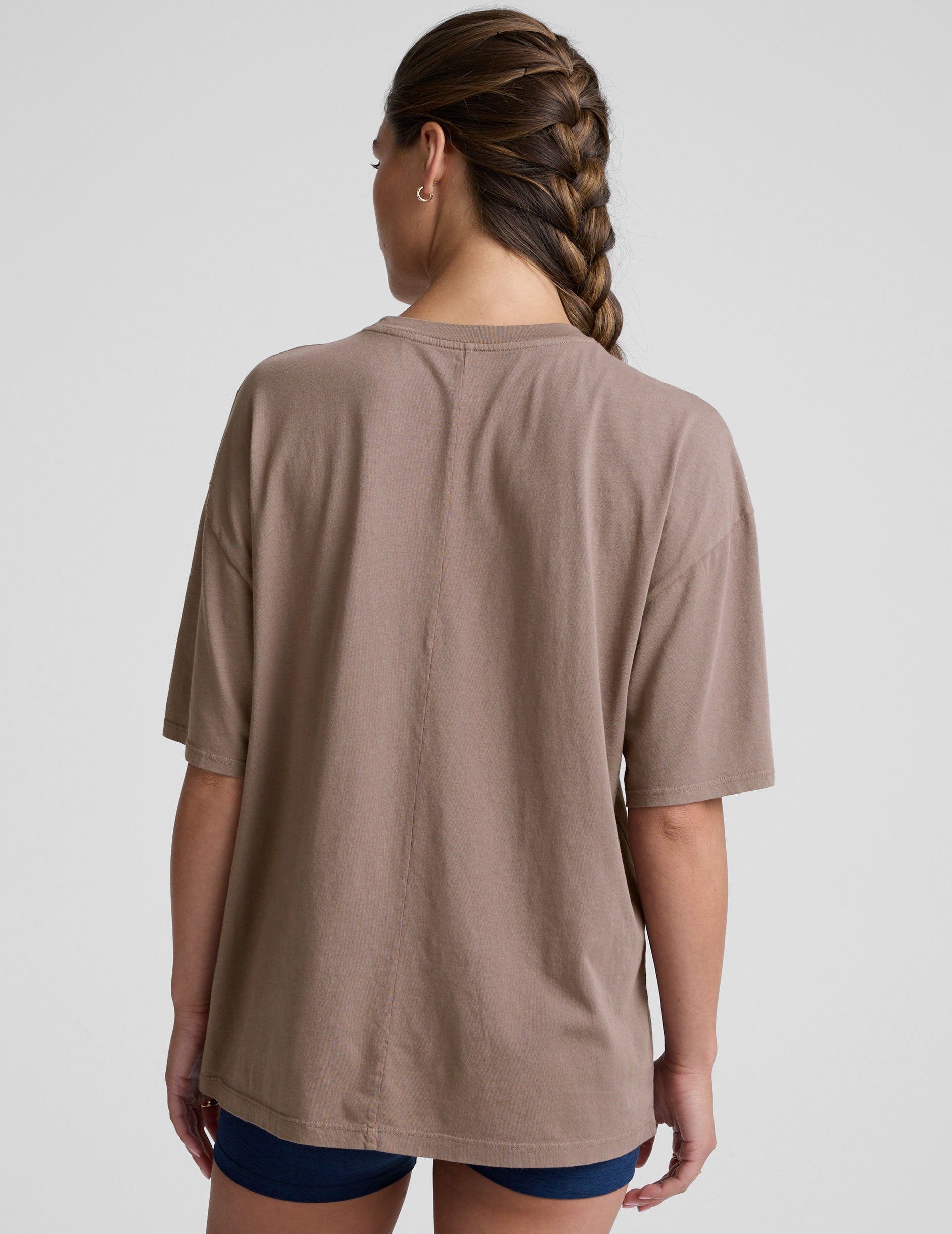 model wearing a brown oversized cotton t-shirt and navy shorts on a light gray background.