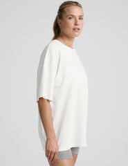 model wearing a white oversized cotton t-shirt and grey shorts against a plain background.