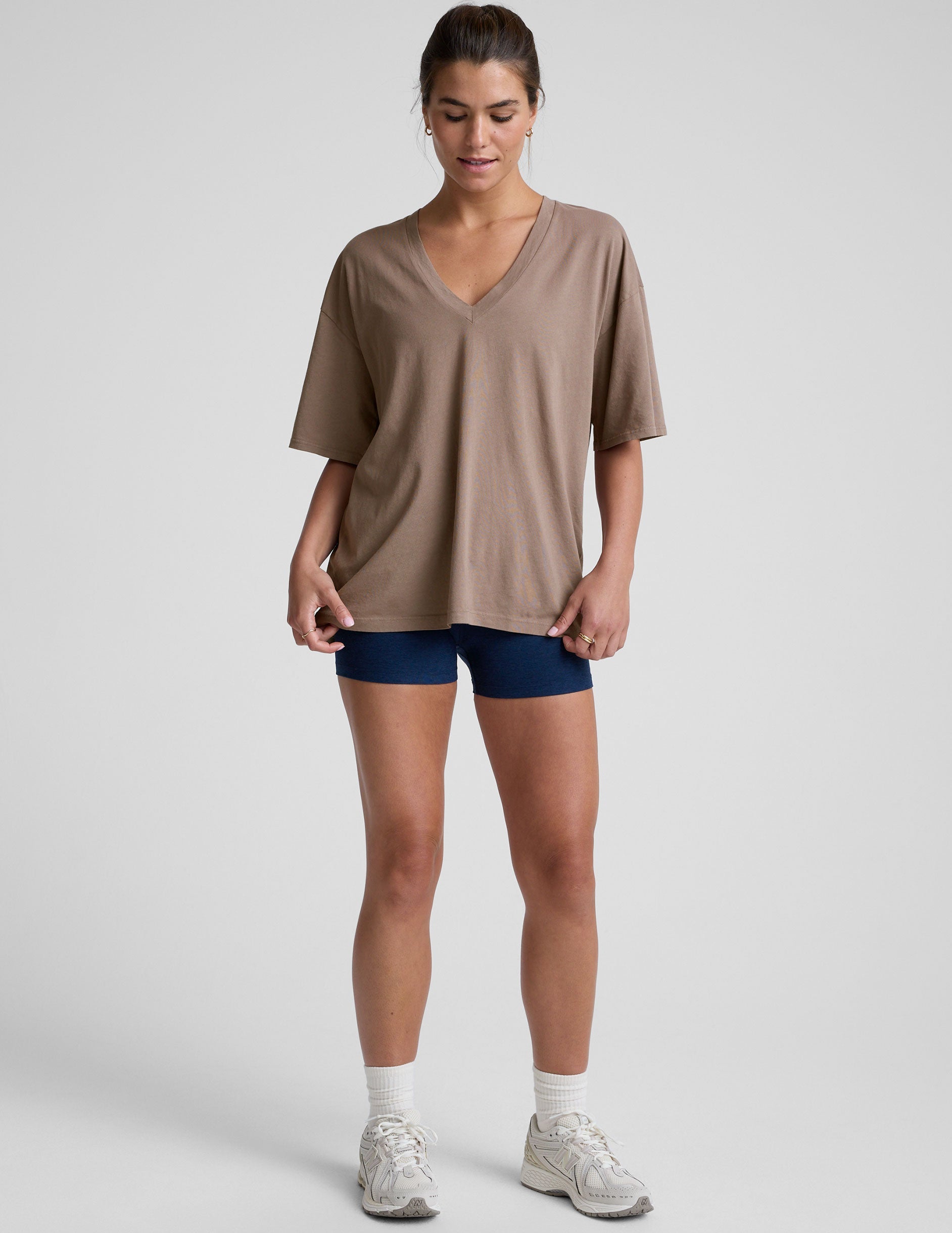 model wearing a brown oversized v-neck top and blue shorts on a plain background.