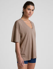 model wearing a brown oversized v-neck top and blue shorts on a plain background.