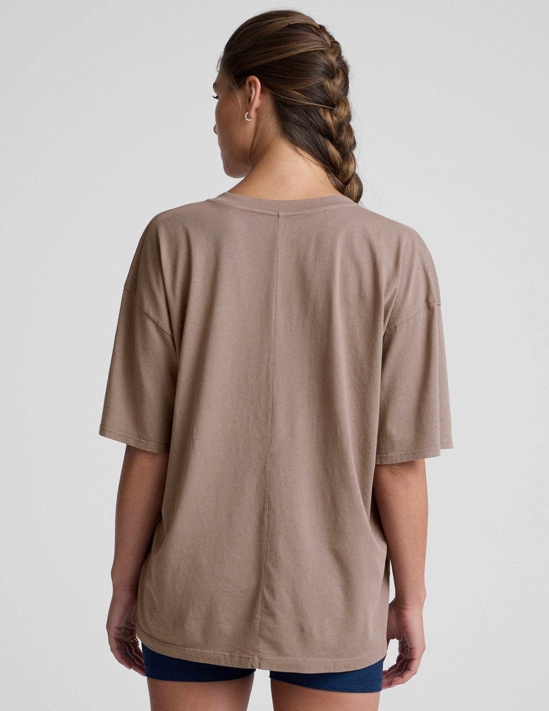 model wearing a brown oversized v-neck top and blue shorts on a plain background.