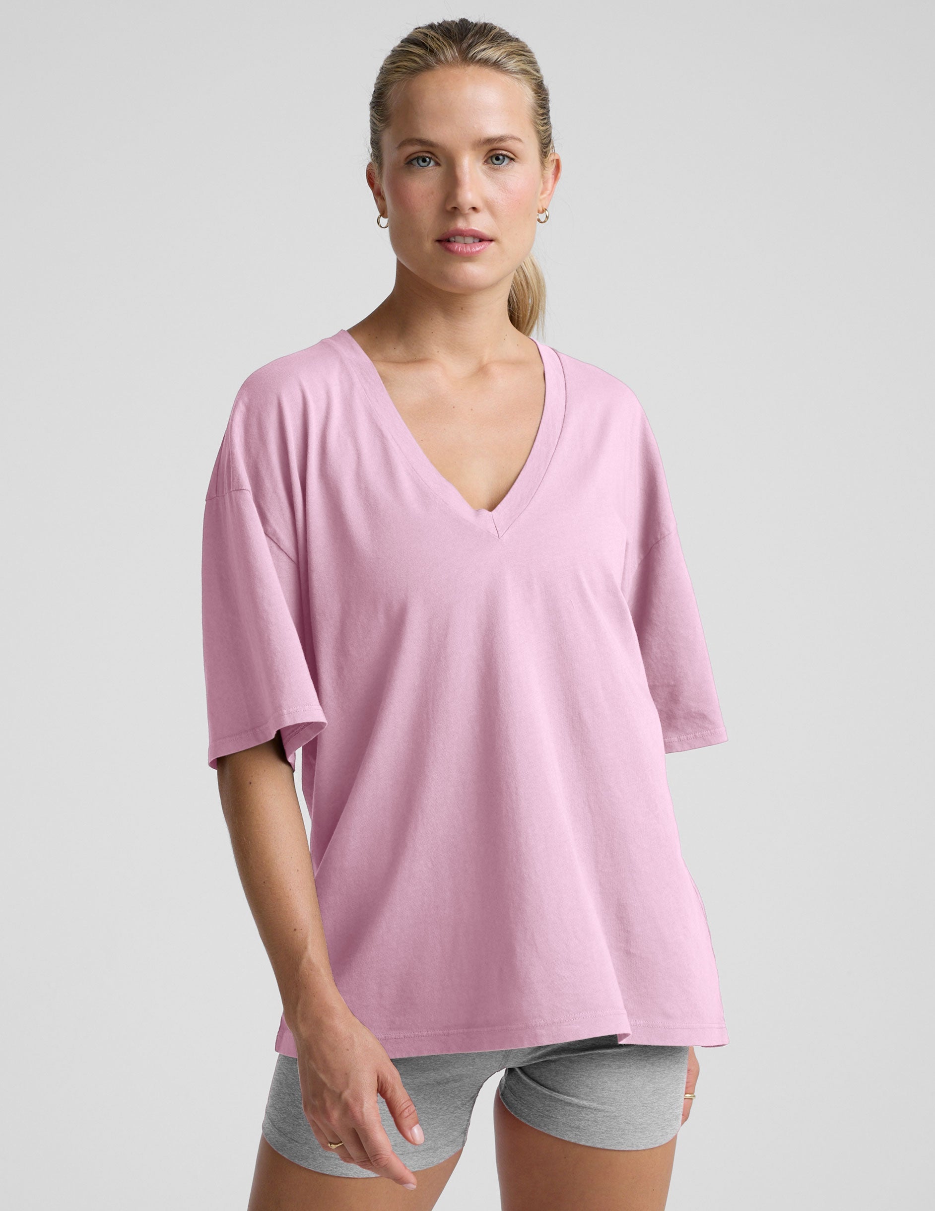 model wearing a pink oversized v-neck top and gray shorts on a plain background.