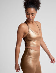 woman wearing a gold v-neck cropped tank and leggings on a plain background.