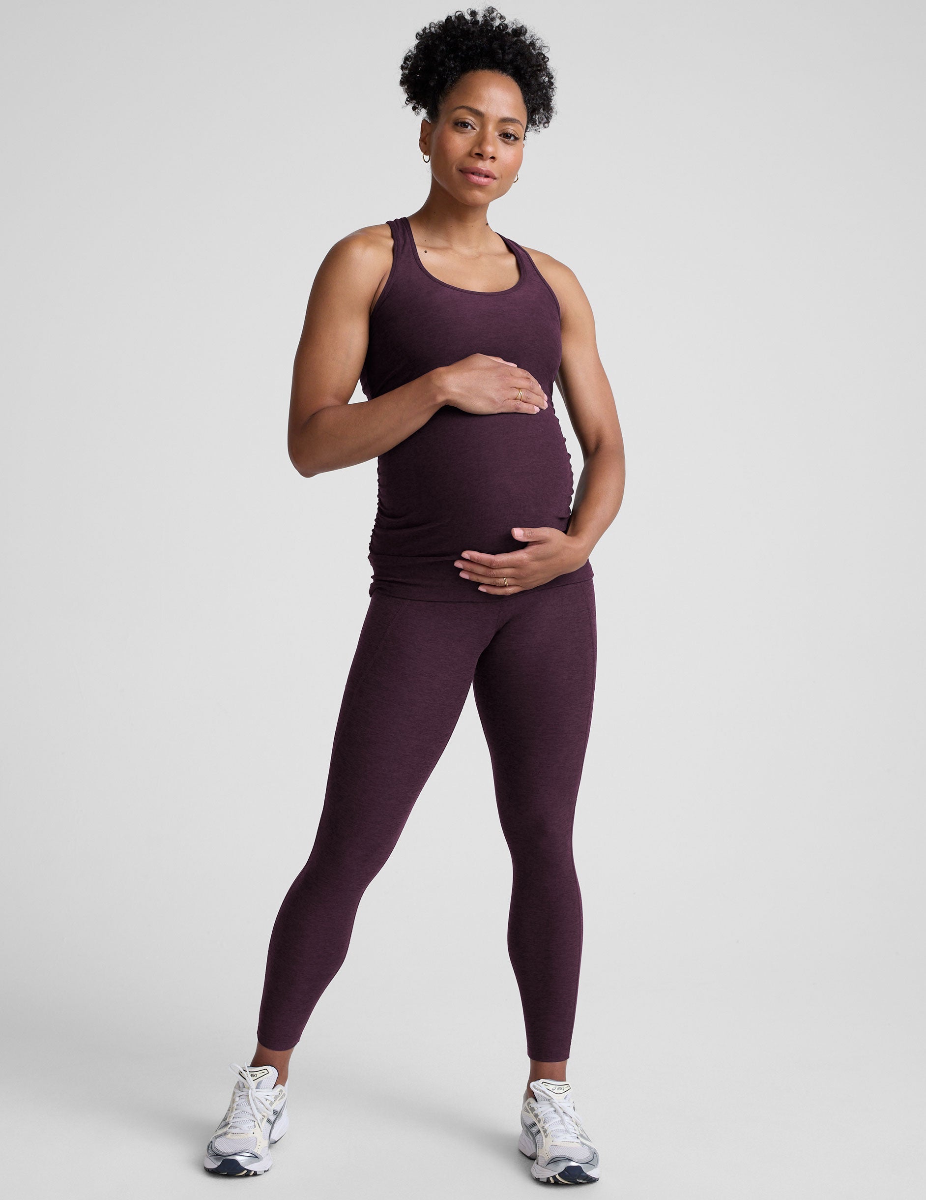 model wearing a purple maternity racerback tank top and leggings against a gray background.