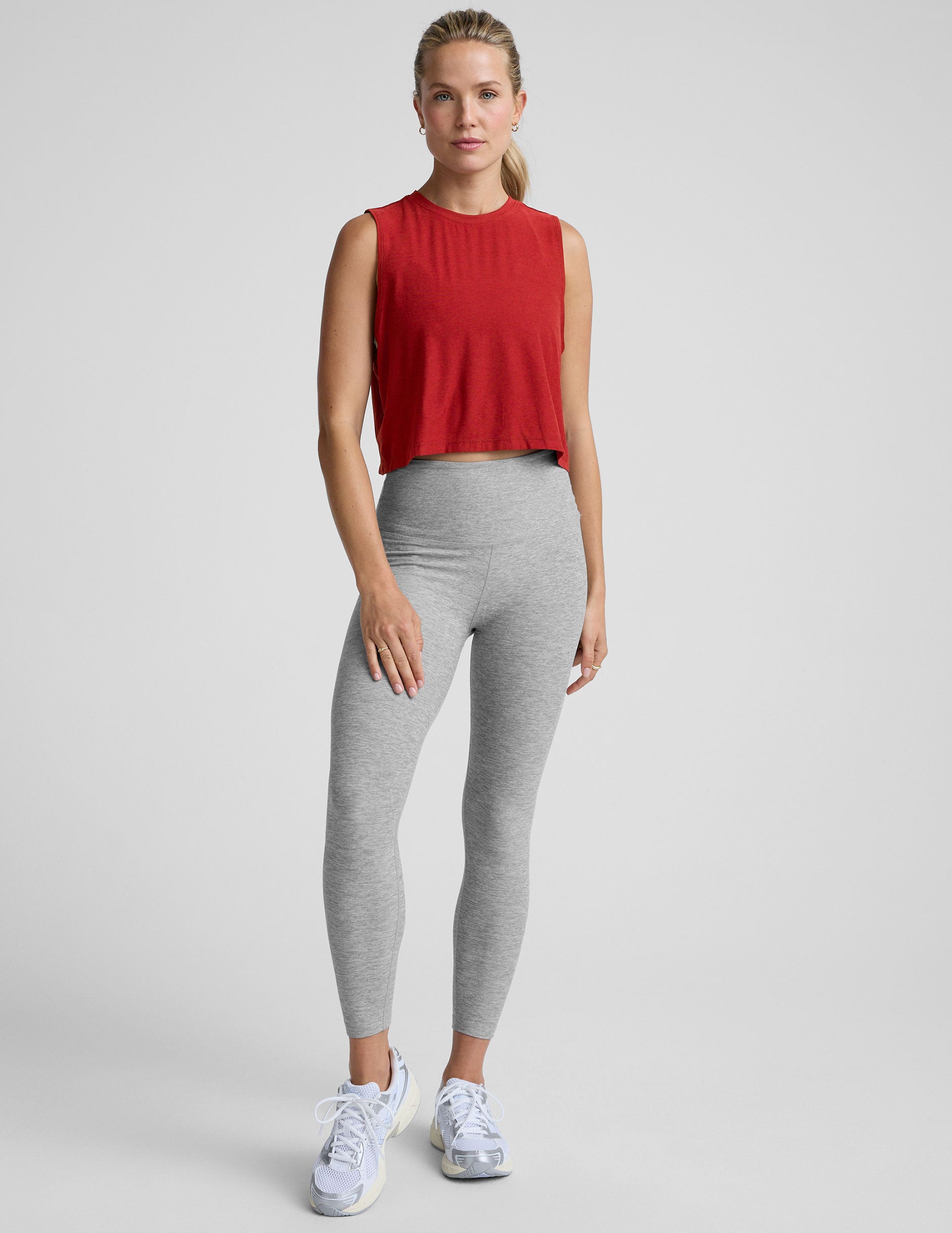 model wearing a red sleeveless top and gray leggings on a plain background.