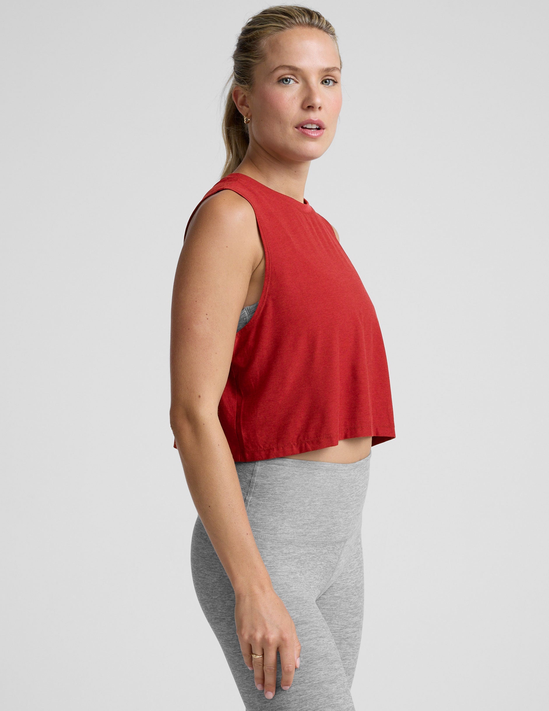 model wearing a red sleeveless top and gray leggings on a plain background.