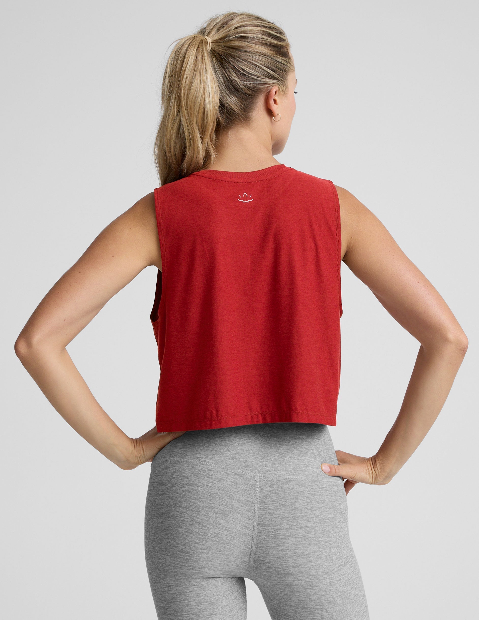 model wearing a red sleeveless top and gray leggings on a plain background.