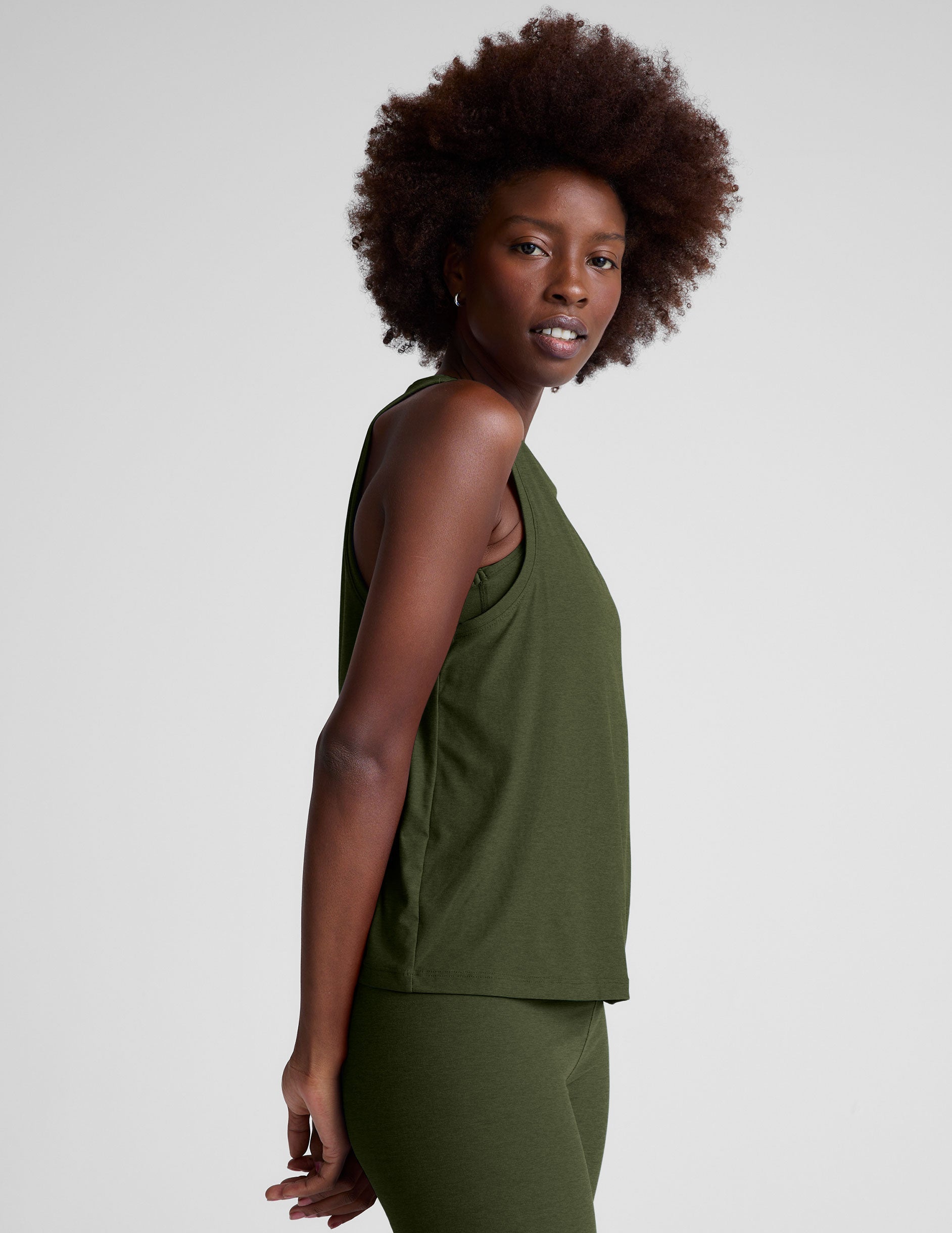 model wearing a green scoop neck tank top and leggings against a plain background.