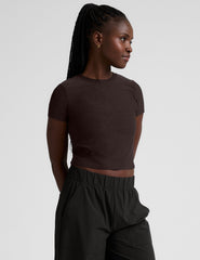 model wearing a brown crop top and black pants against a plain background.