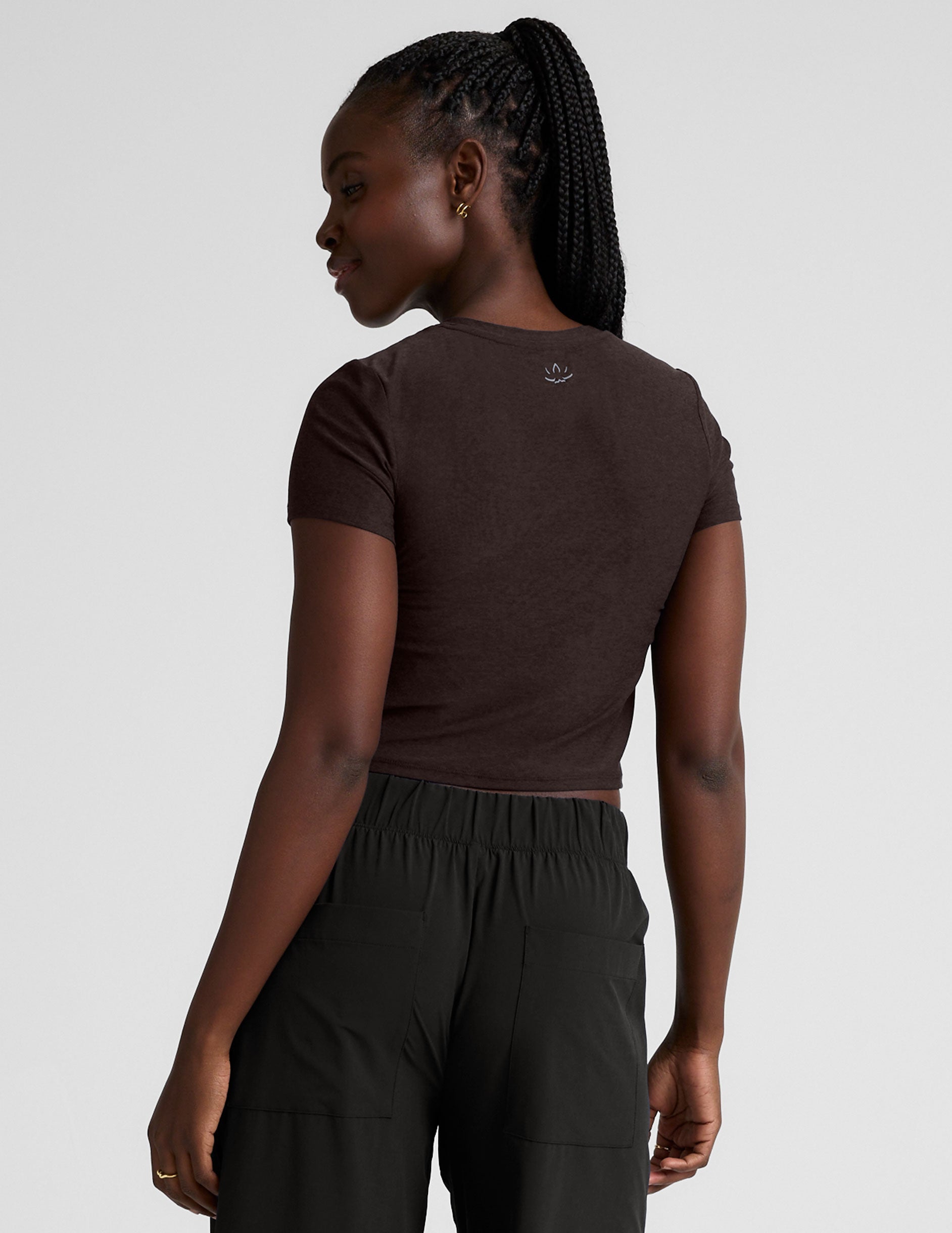 model wearing a brown crop top and black pants against a plain background.
