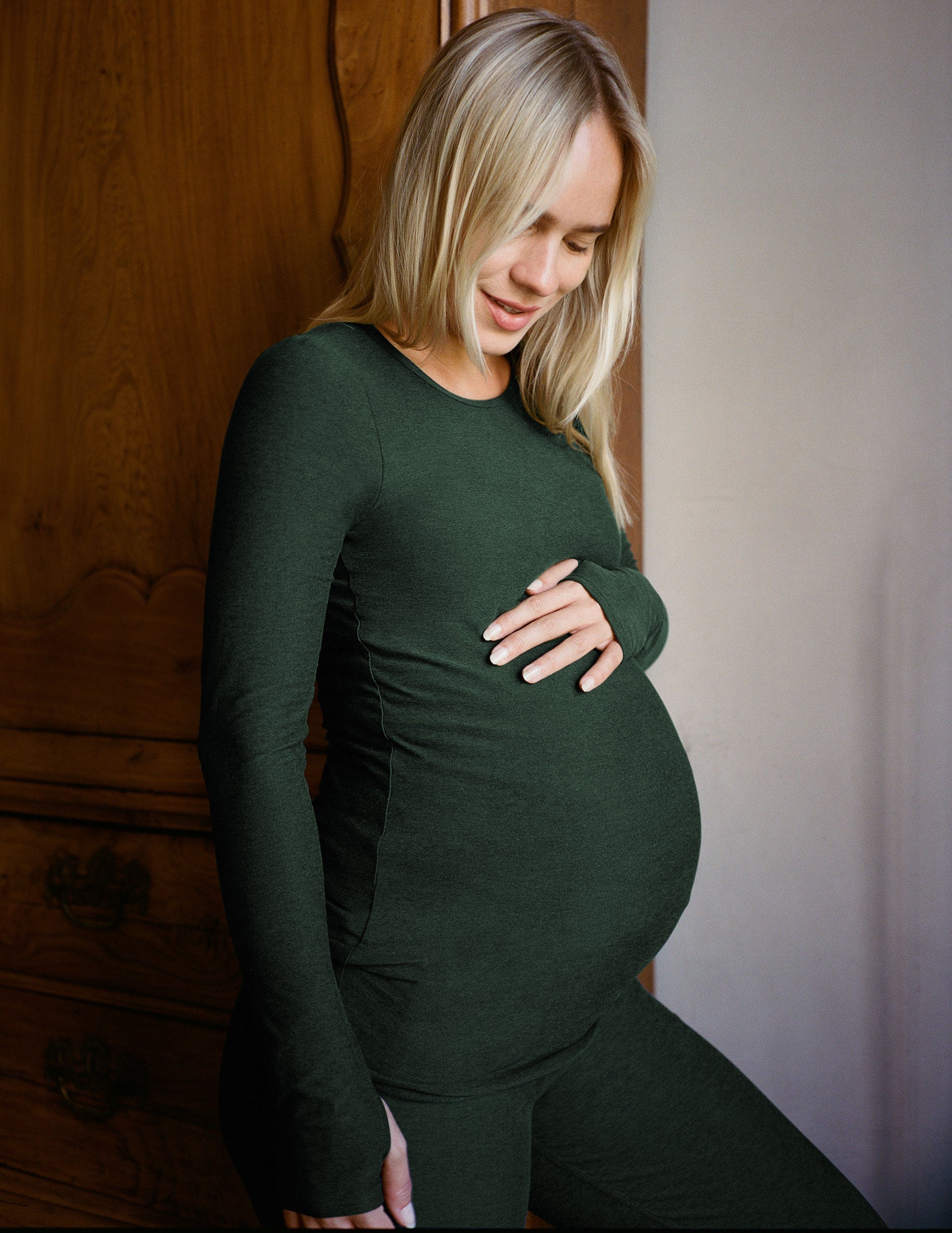 model wearing a green long-sleeve maternity top and leggings against a plain background.