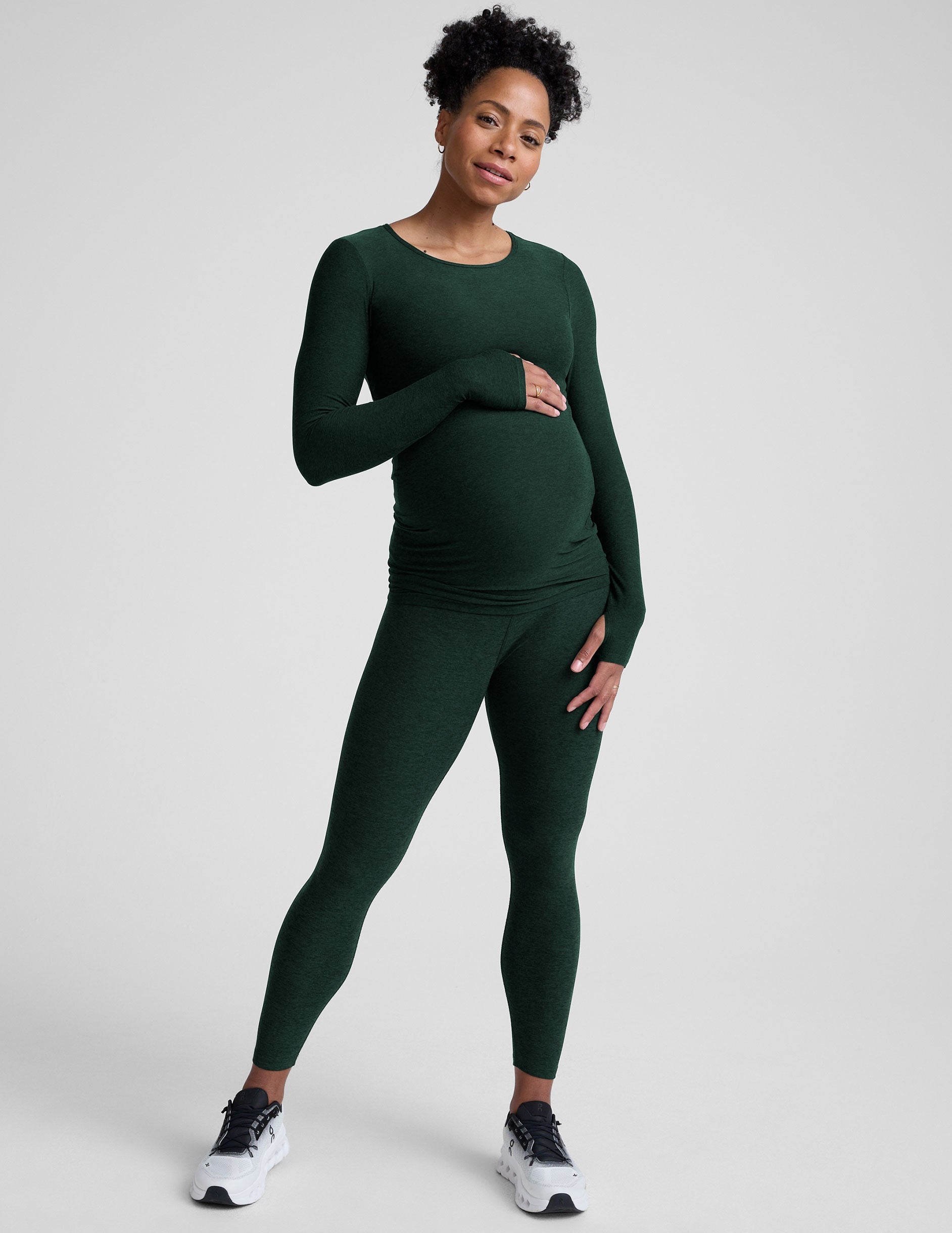 model wearing a green long-sleeve maternity top and leggings against a plain background.