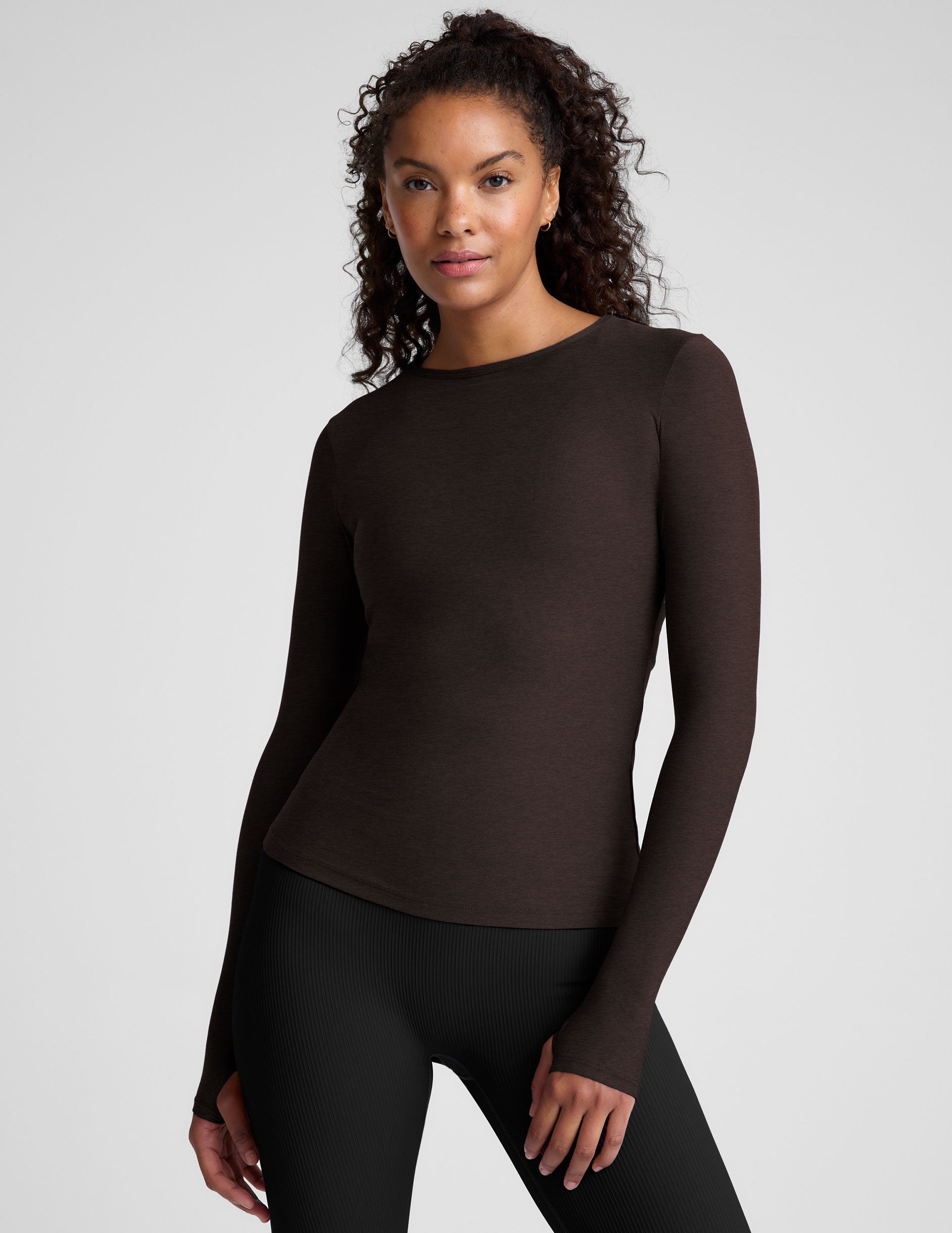 Woman wearing a brown long-sleeve top and black leggings on a plain background.