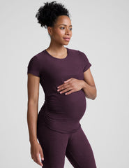 model wearing a purple maternity t-shirt and leggings against a light gray background.