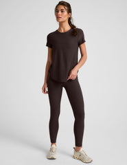 woman wearing a brown t-shirt and leggings on a light gray background.