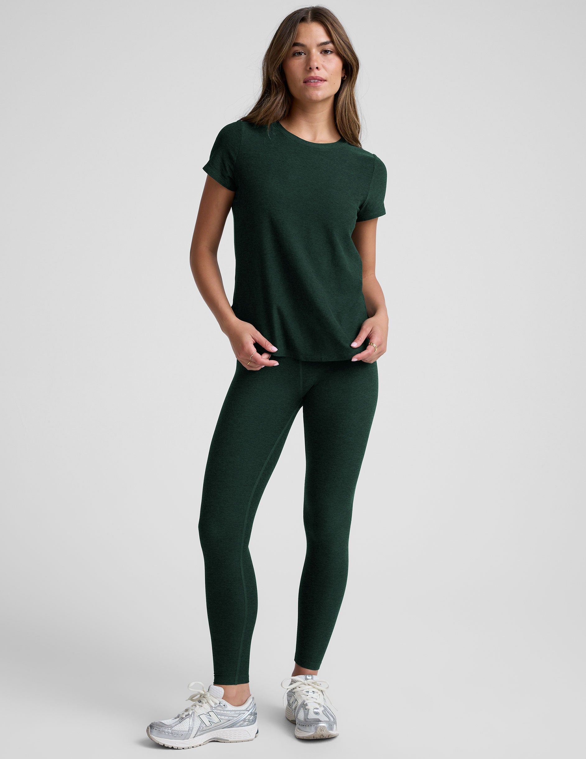 woman wearing a dark green t-shirt and leggings against a plain background.