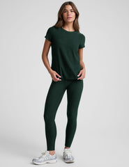 woman wearing a dark green t-shirt and leggings against a plain background.