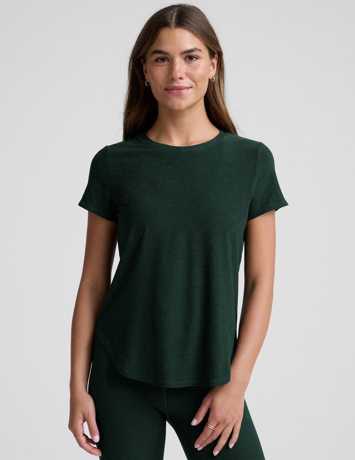 woman wearing a dark green t-shirt and leggings against a plain background.
