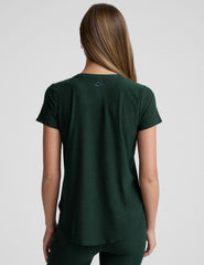 woman wearing a dark green t-shirt and leggings against a plain background.