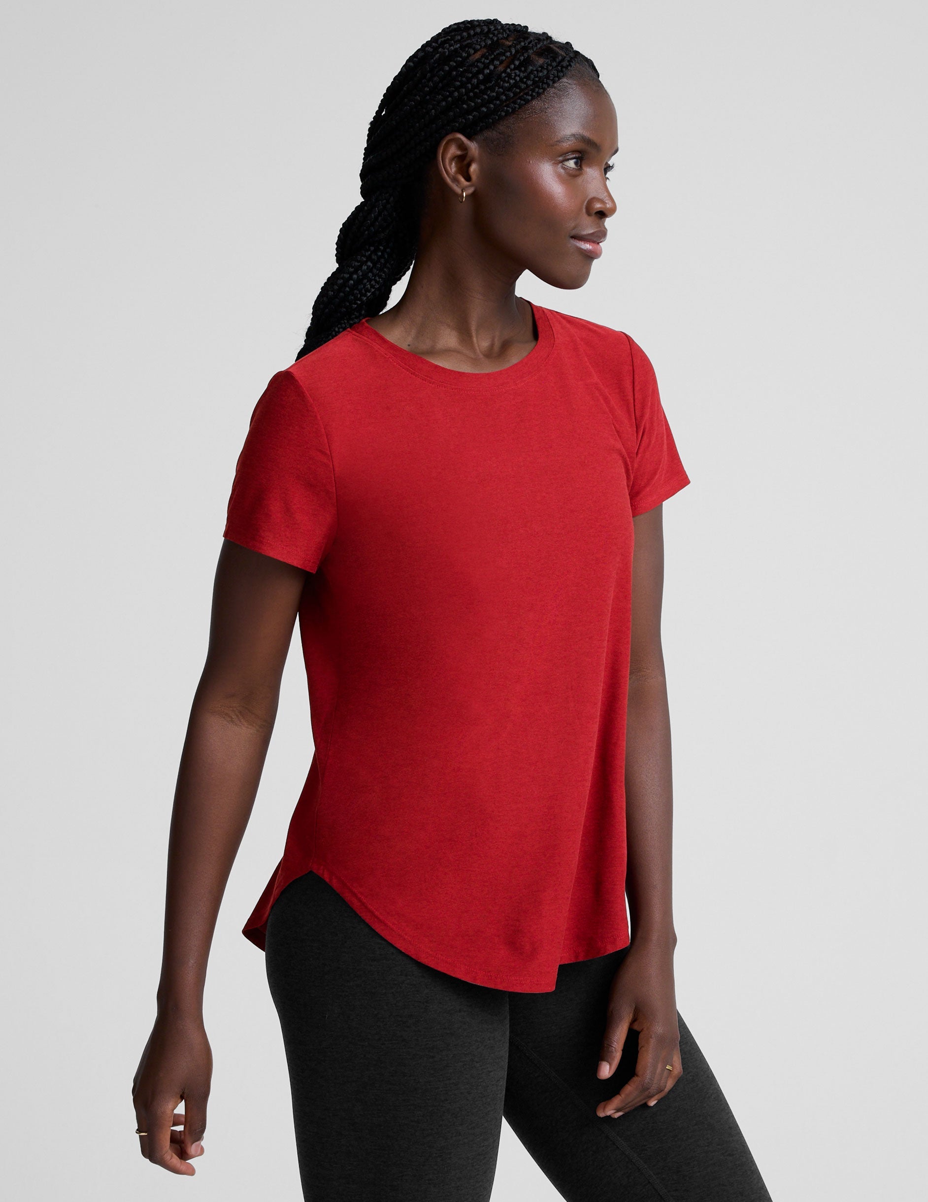 woman wearing a red t-shirt and dark pants on a light gray background.
