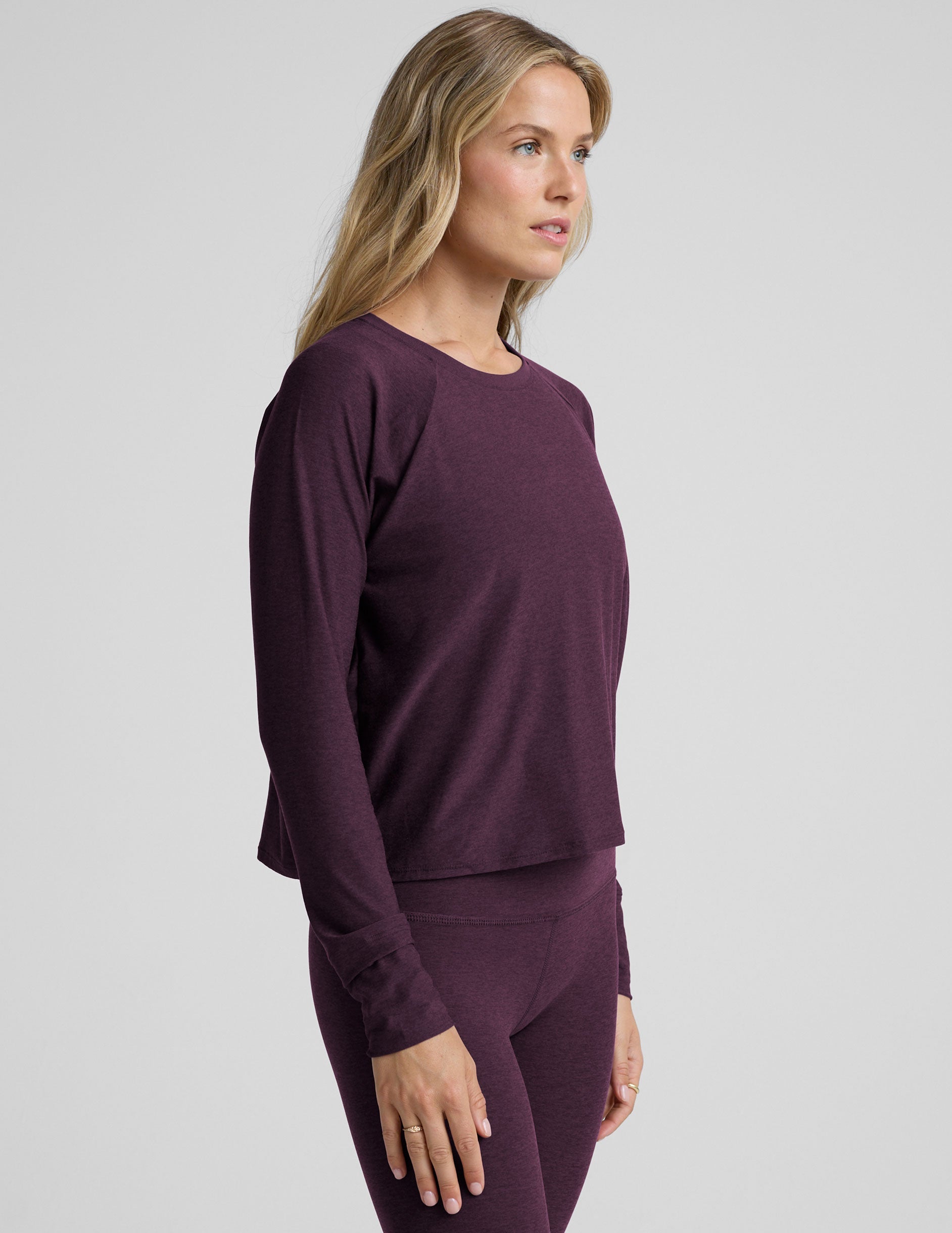 model wearing a purple scoop neck long-sleeve top and leggings on a light gray background.